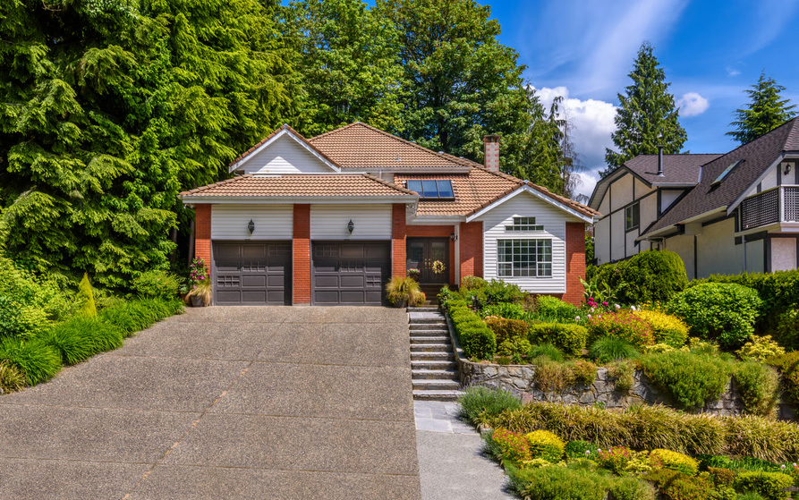 Single-family home in Washington featuring red brick and white siding, a two-car garage, and tiered stone-wall landscaping on a sloped driveway.