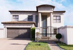 Two-story modern beige stucco home with garage, paved driveway, and gated entrance.