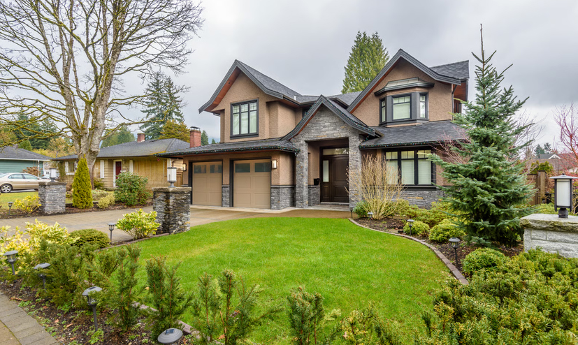 Exterior of a multi-story craftsman home with a two-car garage and manicured front lawn under an overcast sky.